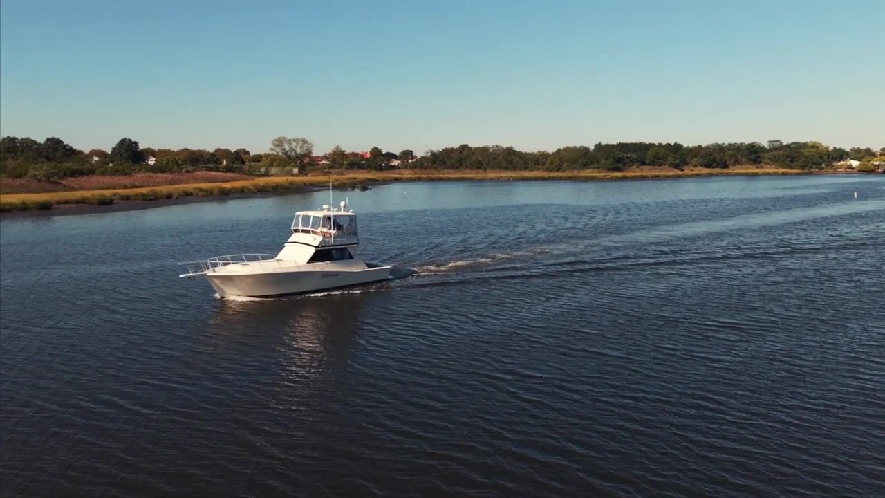 Luftaufnahme des Belt Pkwy, der einen Bach in Brooklyn überquert. Die mehrspurige Fahrbahn überspannt das Wasser bei leichtem Verkehr. Städtische Infrastruktur über der Natur. Die Kamera fährt heran, schwenkt nach unten und nach links
