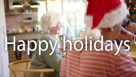 animation of happy holidays text over diverse senior friends sitting at table at christmas