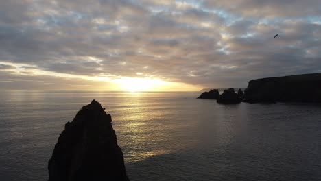 Aerial-static-shot-of-sunset-on-sea-stack-and-coastline-with-bird-flying-past