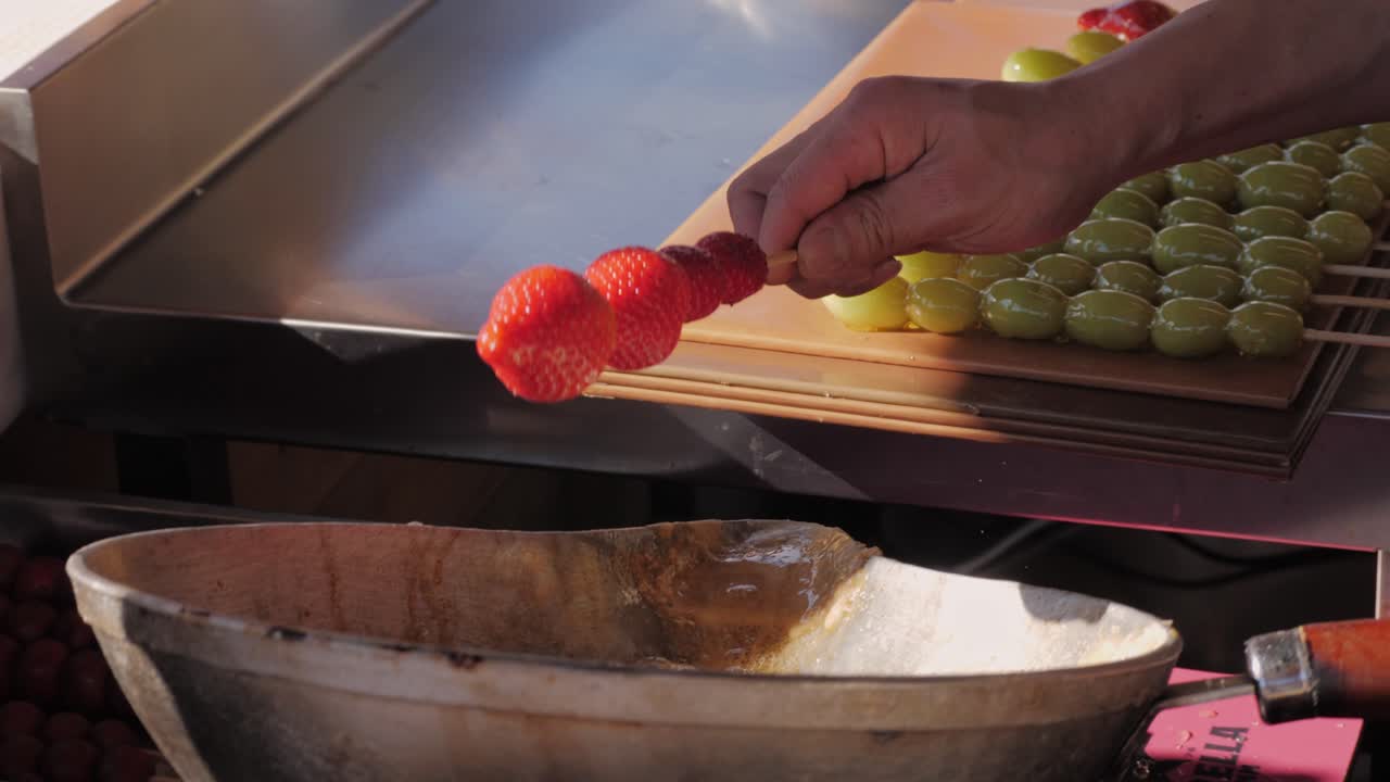 Making fruits in boiling caramel close-up. Chinese winter sweet dessert Tanghulu street food.Berries, grapes, tangerine and others fruit caramelized in sugar. Asian street market with traditional food.. High quality 4k footage