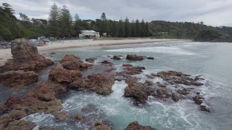 Raue-Felsen-Und-Brechende-Wellen-Am-Flynns-Beach-Mit-Blick-Auf-Das-Strandcafé-In-New-South-Wales,-Australien