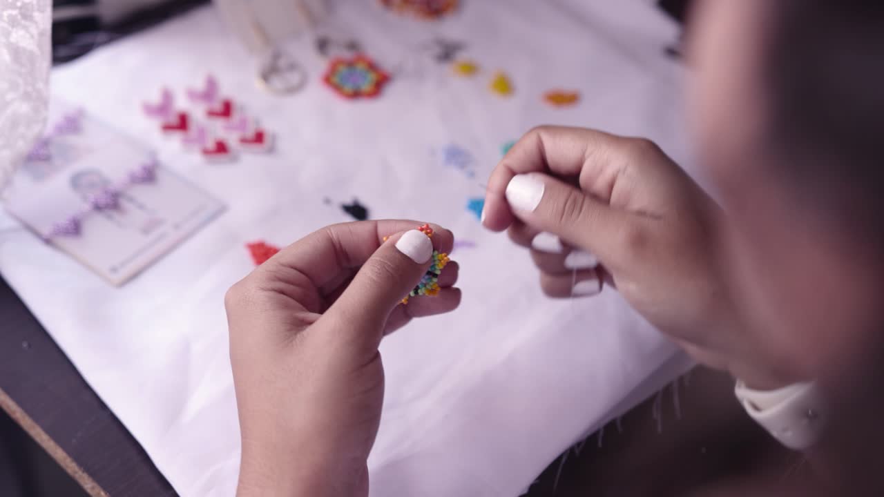 Closeup of woman&acute;s hands making crafts with colorful little beads, needle and thread 003