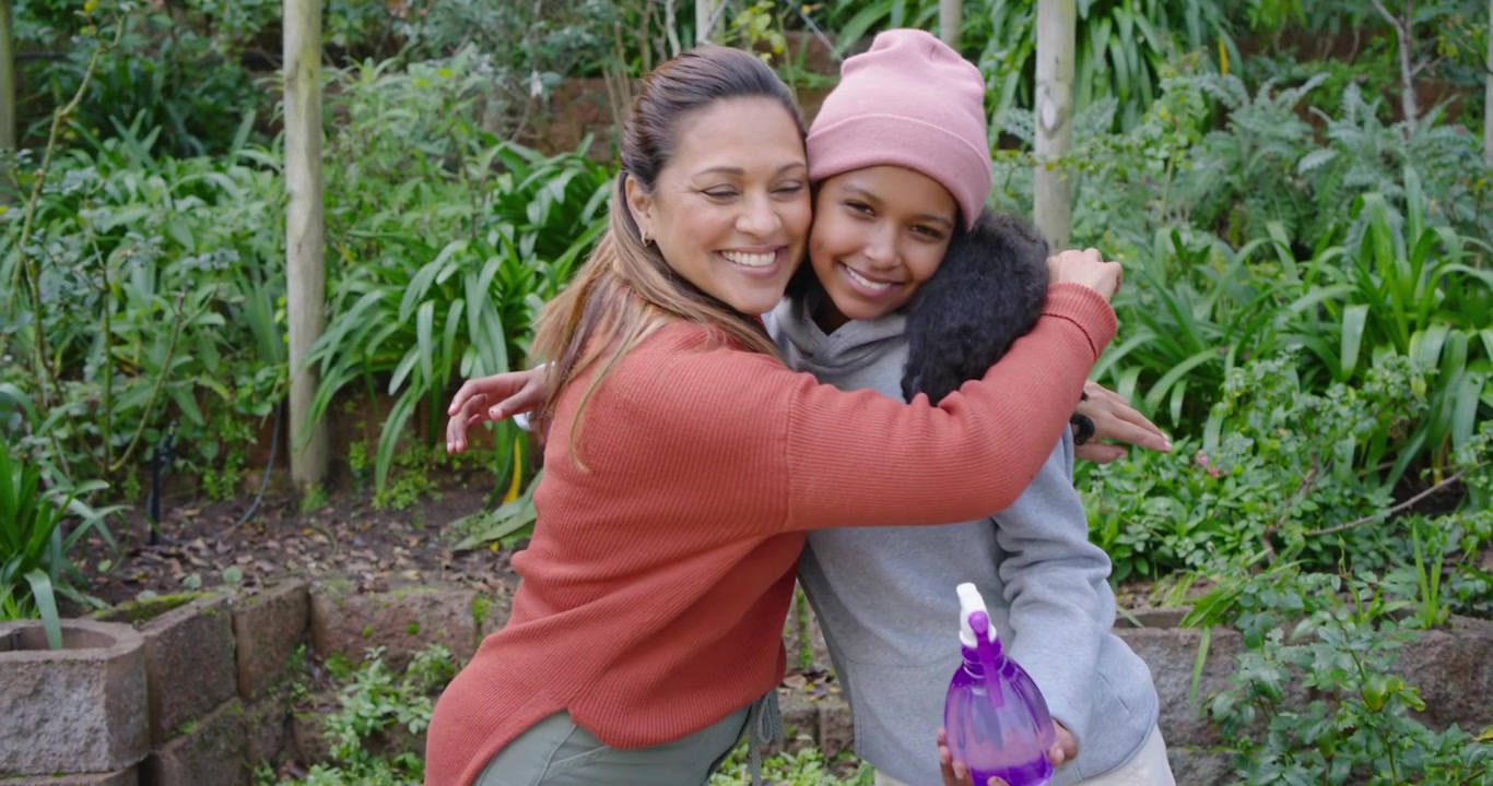 Mamma afroamericana che guida l'adolescente mentre controllano e piantano a un tavolo da giardino, con uno spruzzino viola.
