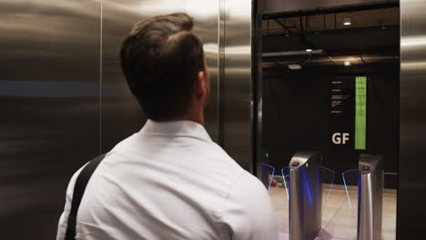 Riding elevator, businessman in white shirt facing door, carrying shoulder bag