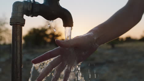 frau wäscht die hand unter dem wasserhahn auf einem ländlichen bauernhof bei sonnenuntergang süßwasser fließt aus dem wasserhahn