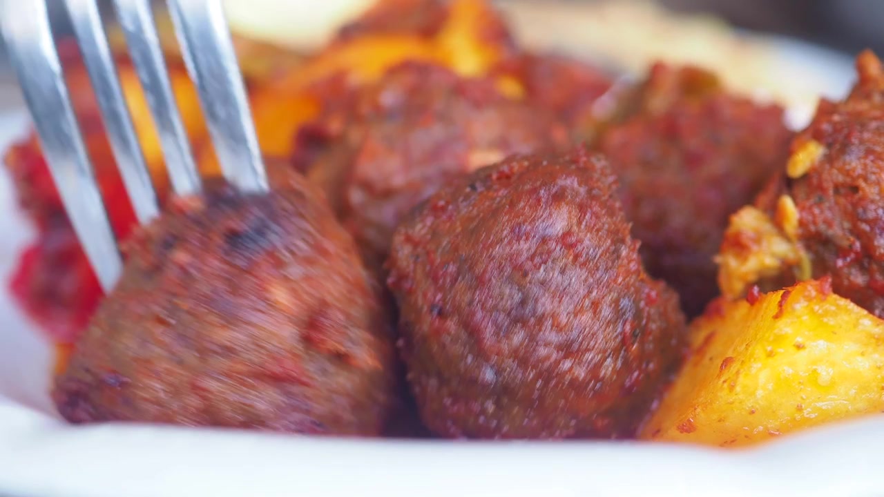 Primo piano di una forchetta che prende una polpetta e patate