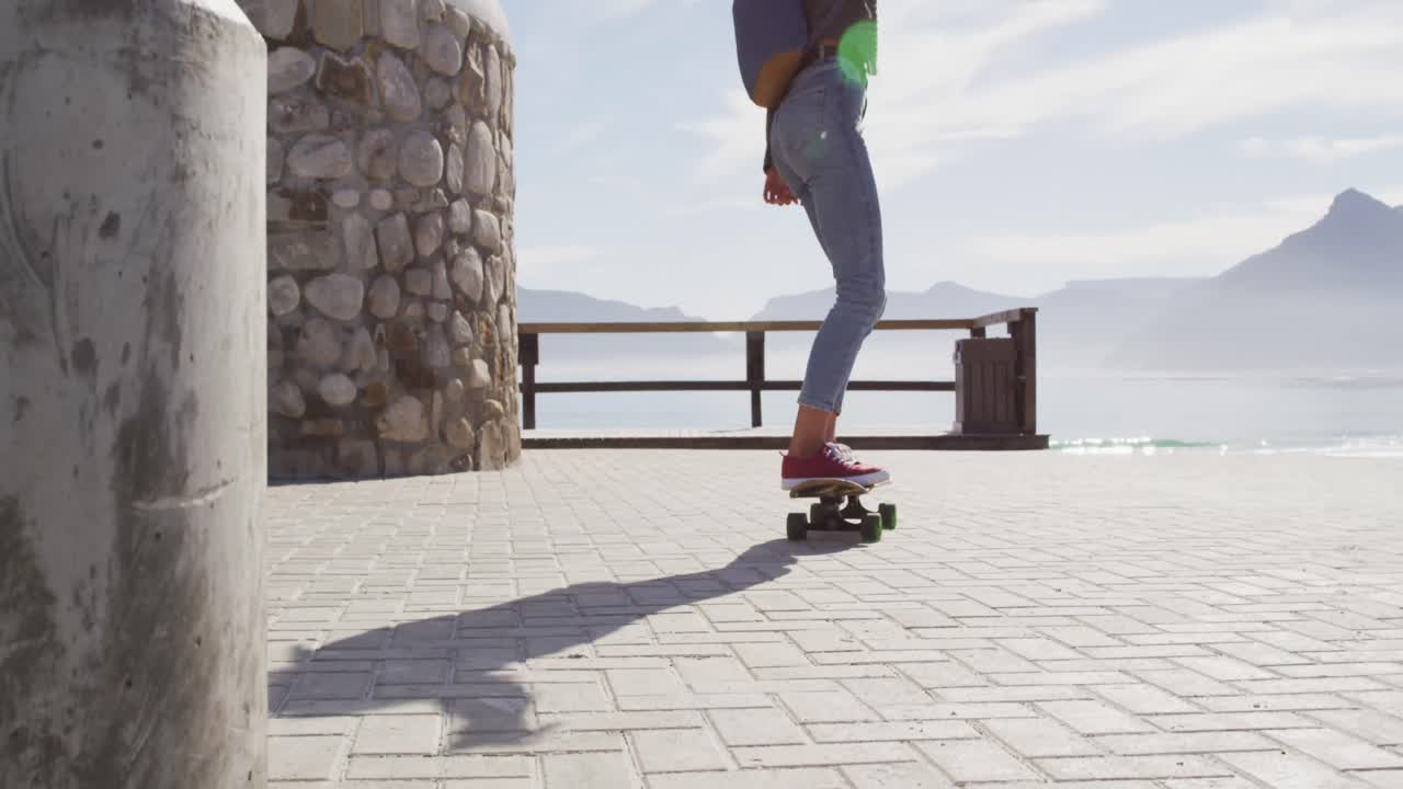vista trasera de una mujer de raza mixta patinando en un soleado paseo marítimo junto al mar