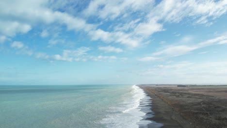 Aerial-reverse-above-breaking-waves-at-vast-Kaitorete-Spit-with-turquoise-colored-South-Pacific-Ocean