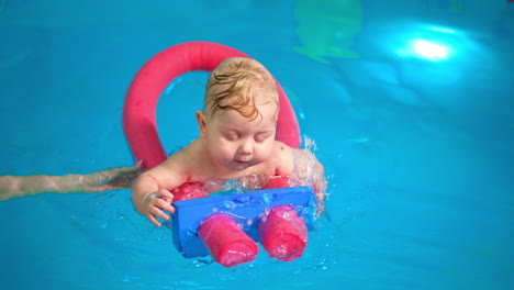 lovely caucasian baby swims with a pool noodle in the swimming pool. female hand supporting the kid.