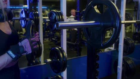 chica en el gimnasio poniendo pesas en la barra con guantes preparándose para entrenar la fuerza de sus brazos