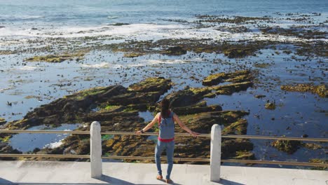 mujer afroamericana de pie en el paseo marítimo por el mar