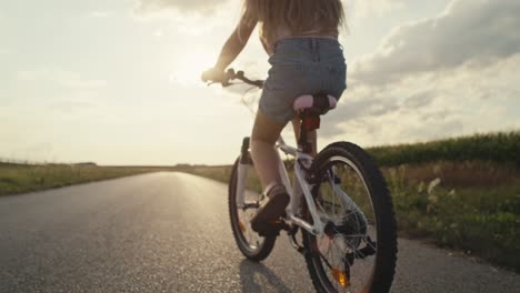 close up of unrecognizable little caucasian girl riding a bike bike at sunset time.