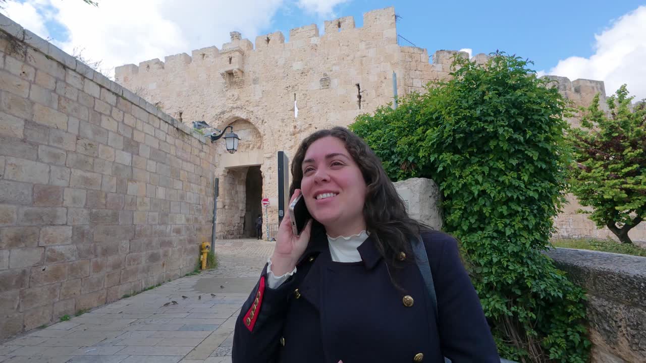 Young adult woman talking on phone near Jerusalem old city walls, Zion Gate. Slow motion.