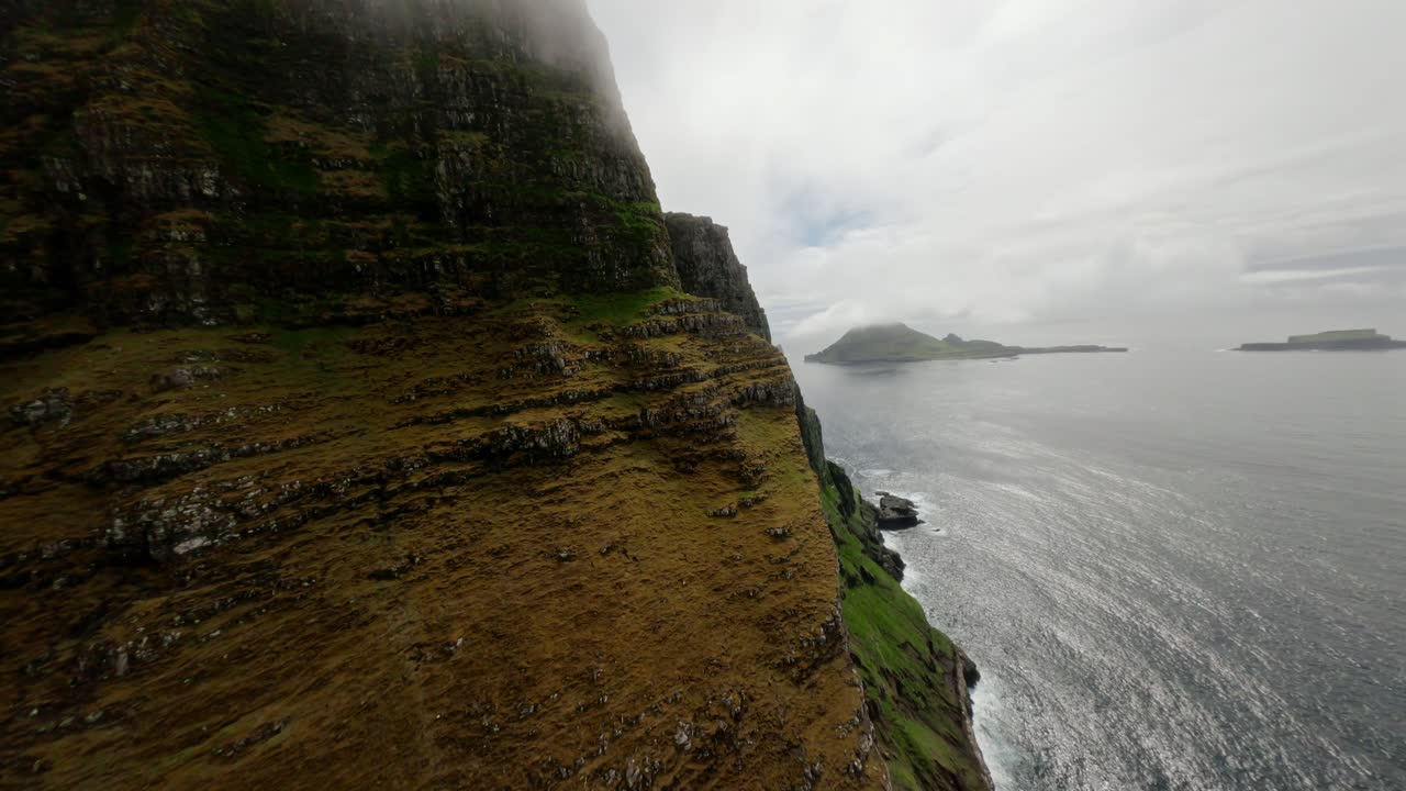 acantilado escarpado de las islas feroe, atmósfera brumosa, islas visibles, filmado por un dron fpv, vista aérea