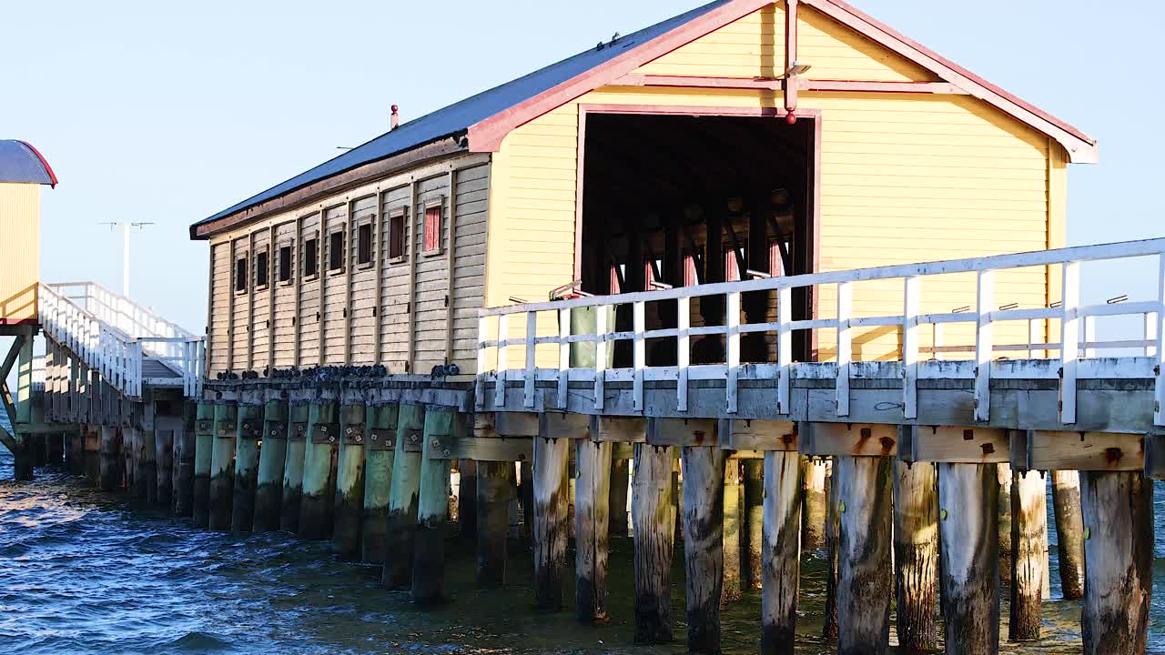 A serene view of a wooden pier house in Bellarine, Victoria, with gentle waves and bright sunlight