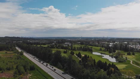 static-wide-drone-view-of-golf-course-lush-green-trees-grass-sand-dunes-ponds-water-aerial-on-sunny-cloudy-dayover-highway-with-light-traffic