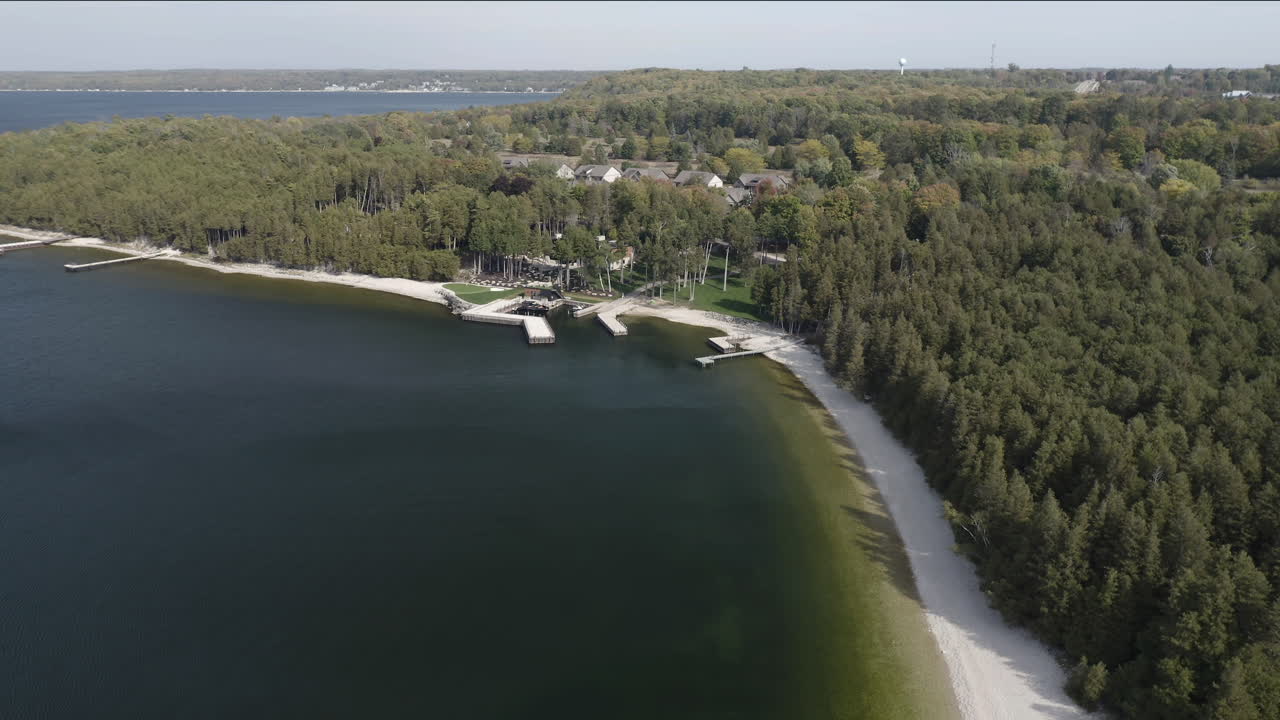 The emerald waters of Pebble Beach meet a stretch of forest and sandy shoreline, where docks extend into the lake and trees blanket the land in tranquil natural harmony