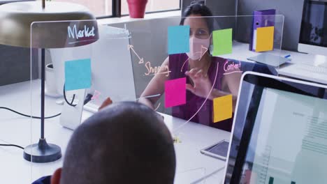 Diverse-business-colleagues-wearing-face-masks-using-computers-talking-in-office