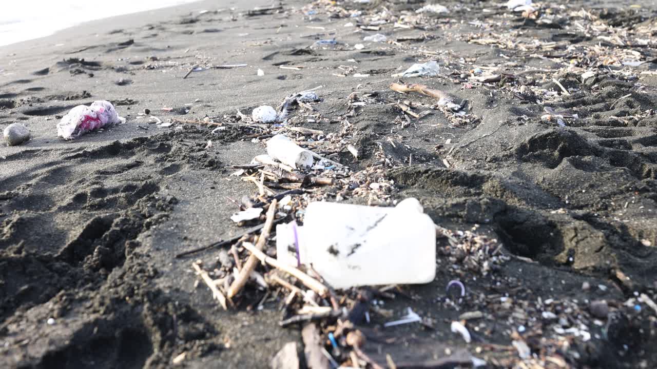 A heavily polluted black sand beach littered with plastic and natural debris