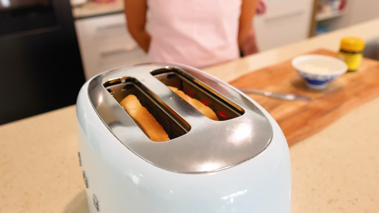 A couple prepares breakfast in a bright kitchen, focusing on a toaster and bread. Warm lighting enhances the cozy atmosphere