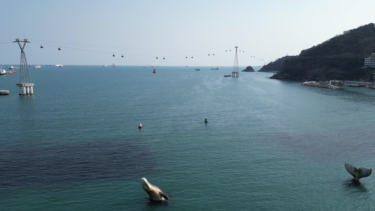 Drone aerial view in South Korea Busan flying over the clear blue ocean with a cable car over it on a sunny day ships on the horizon