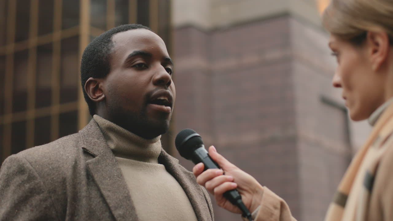 Close-up view of african american man talking and answering to female journalist in the street in autumn