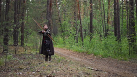 warrior with cape shoots bow looking around in forest