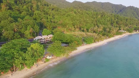 tropical island drone backwards dolly shot of beach resort with lush green rain forest and tropical palm trees with white sand beach and rocky coastline