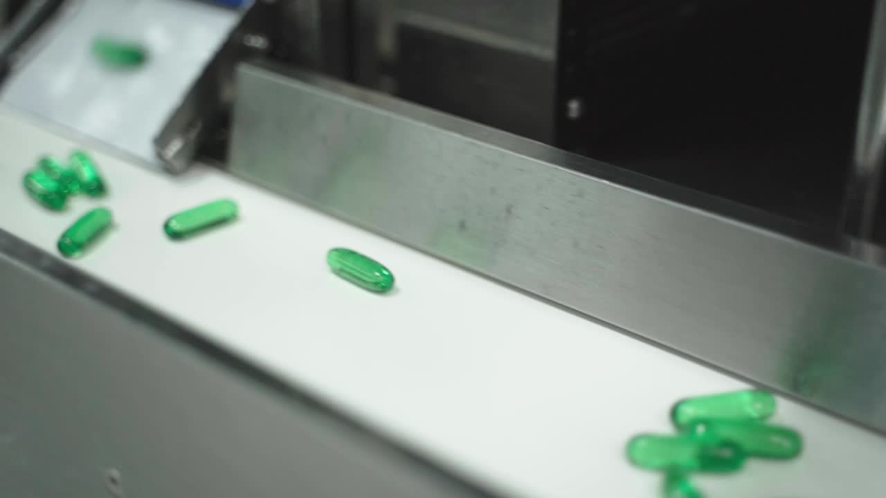 Green capsules falling and moving towards on conveyor belt during pharmaceutical production.