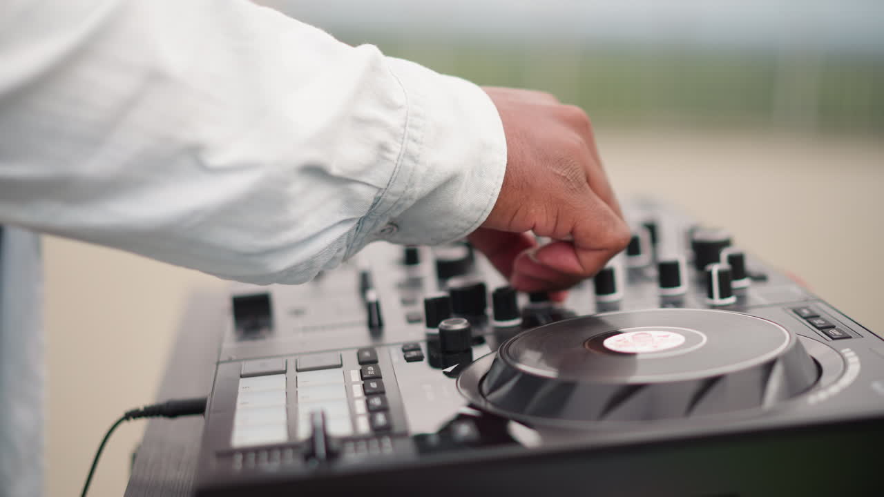 Mani del DJ sul controller, set all'aperto, performance a cielo aperto, rapidi movimenti del fader e regolazioni del jog, transizioni pronte per la folla, cavi e attrezzatura visibili, manica di denim, cielo luminoso, flusso ritmico.