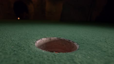 ein orangefarbener minigolfball fällt in das golfloch und springt auf einem golfplatz in die tasche