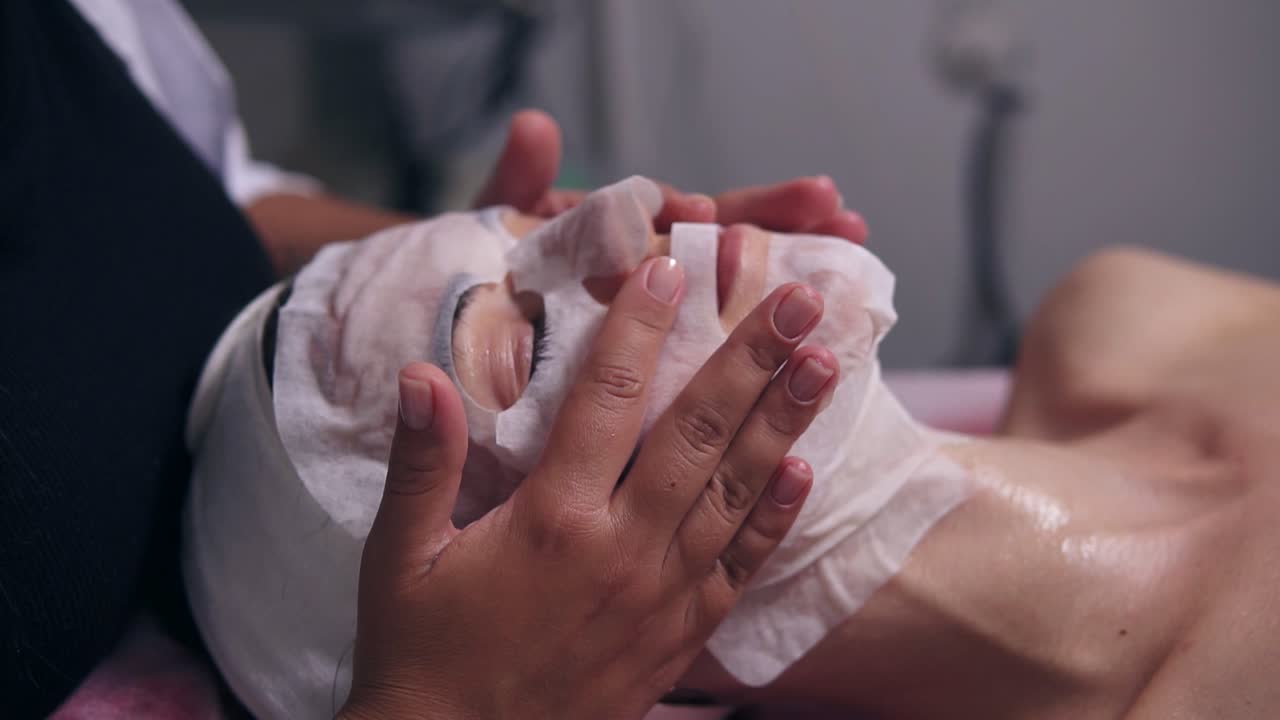 Professional cosmetologist holding her hands on woman's face while applying special mask on female client's face and neck