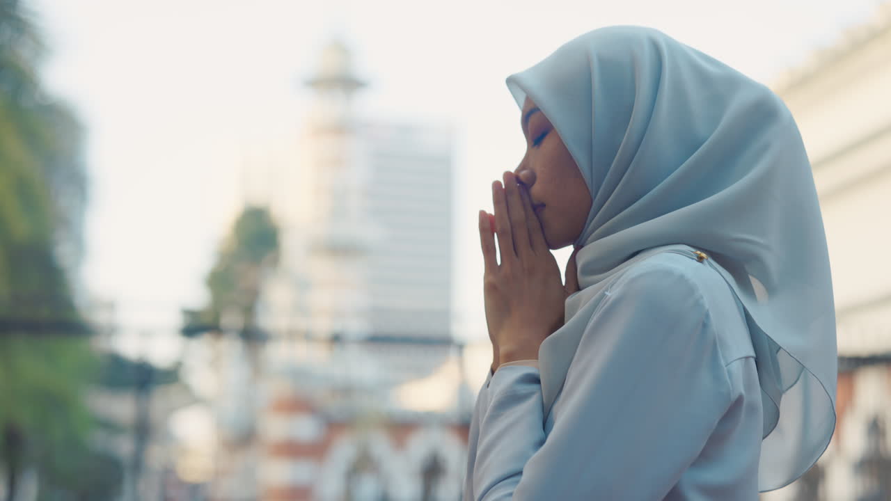 Muslim woman in hijab praying outdoors in a city