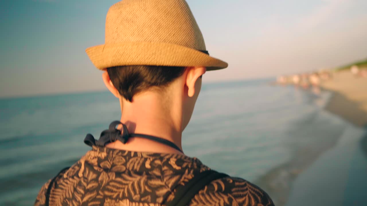 일몰 동안 잔잔한 해변을 걷고 있는 모자를 쓴 젊은 여성의 뒷모습