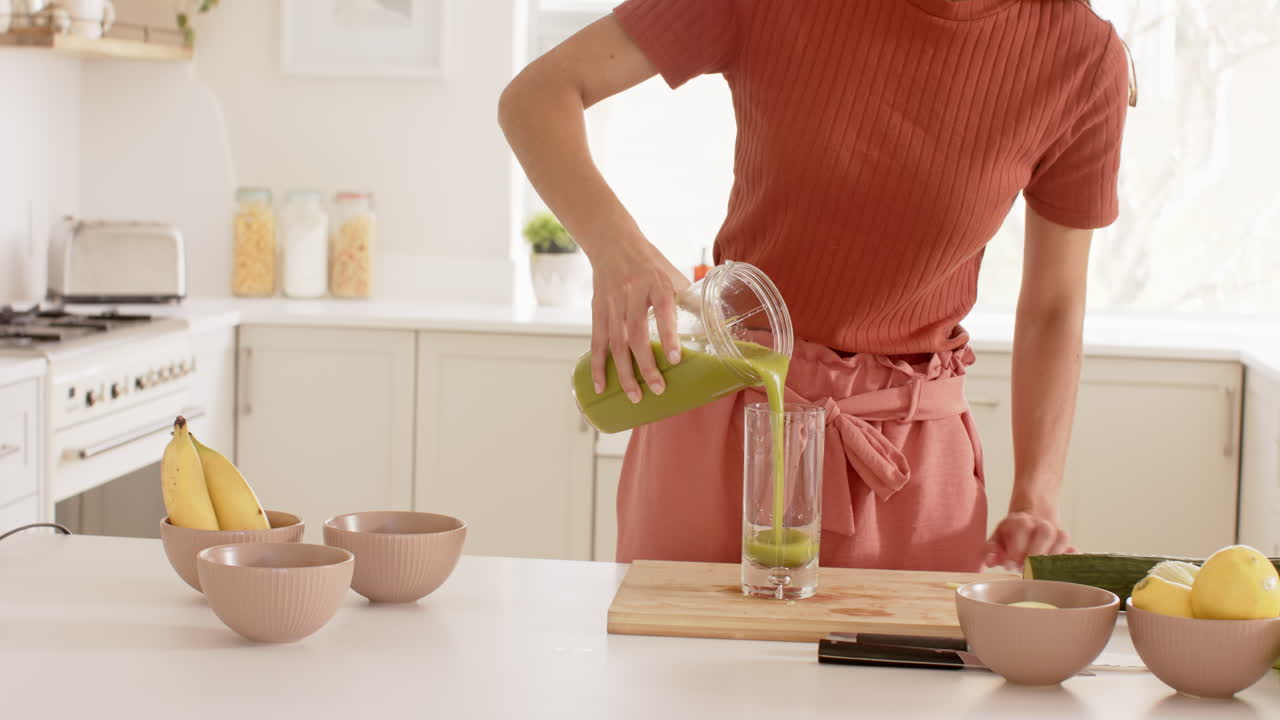 Preparing fresh green smoothie in modern kitchen with bananas and bowls