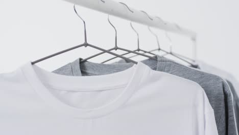 video of white and grey t shirts on hangers and copy space on white background