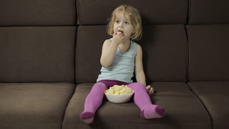 girl sitting on sofa and eating corn puffs. child smiling and taste puffcorns