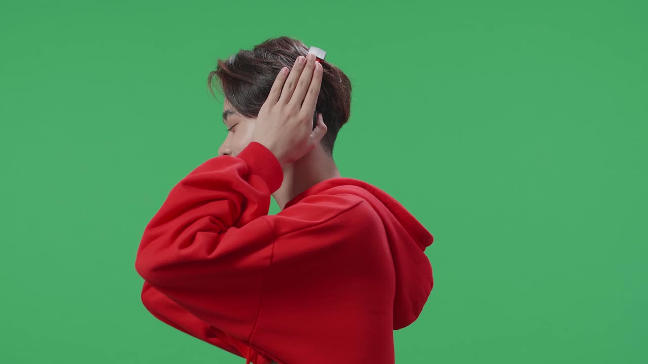 Side View Of Asian Transgender Male Listening To Music With Headphones And Dancing In The Green Screen Studio