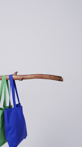 vertical video of blue and green canvas bags hanging from branch with copy space on white background