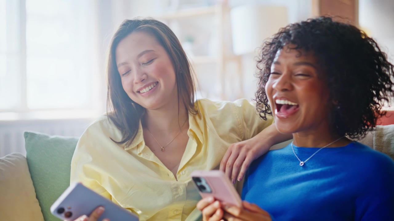 ソファで携帯電話を共有する多様な女の子たちのクローズアップ。友人たちが一緒に閲覧しながら笑っている。
