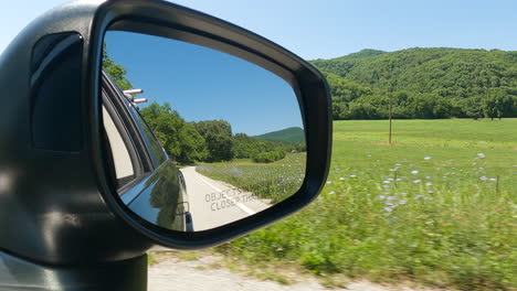 green natural landscape seen through side mirror from car's driver seat