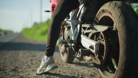 close-up of a biker kickstarting their motorcycle on the roadside, with a car in the distance approaching in the opposite direction