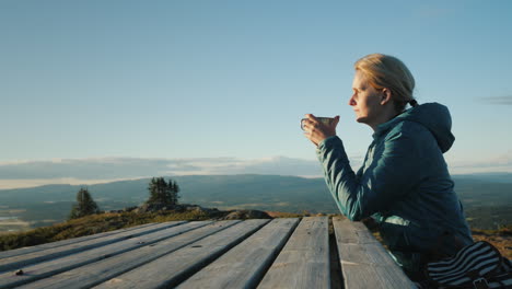 a woman traveler sits at a table high in the mountains drinking tea far from civilization nature of