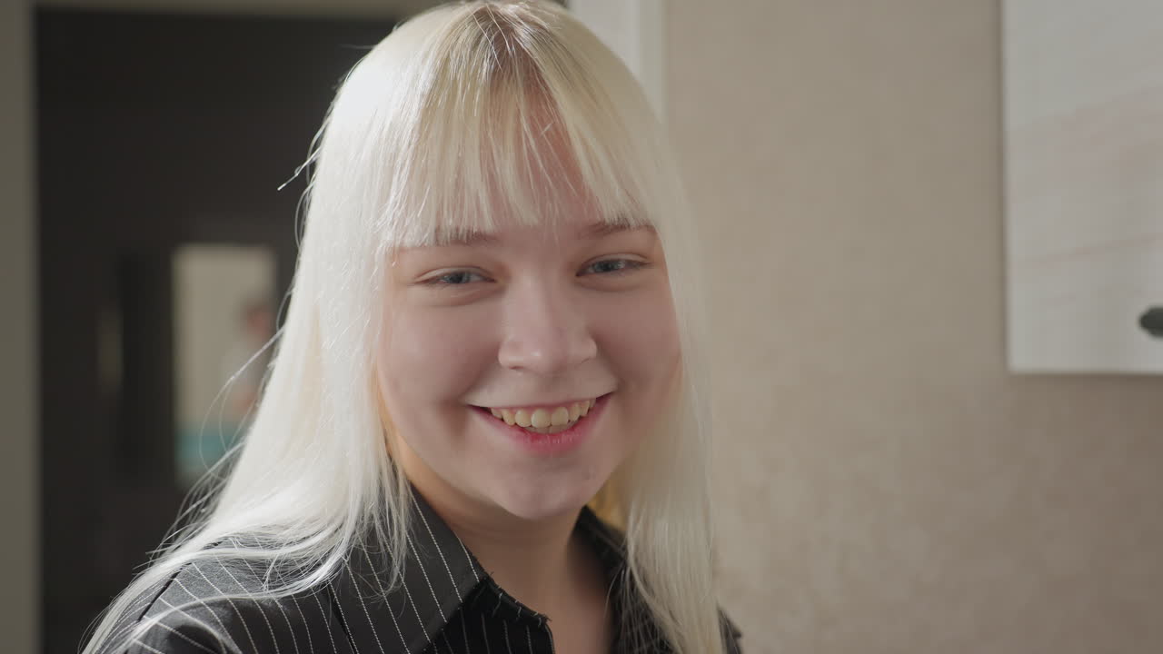young girl with long hair turns to camera smiling warmly while seated on kitchen cabinet soft daylight highlights her features casual outfit and relaxed posture evoke friendly home atmosphere