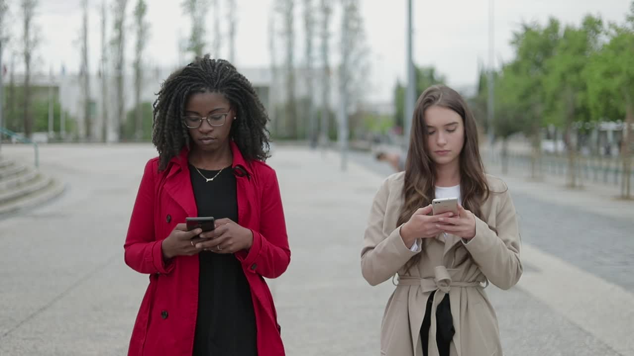 Afro-american and Caucasian women walking, texting on phones