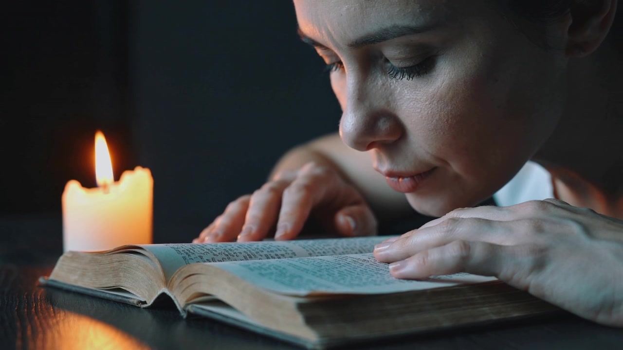 Donna che si sporge in avanti, leggendo un libro antico a lume di candela a tavola, con le dita che tracciano il testo sbiadito.