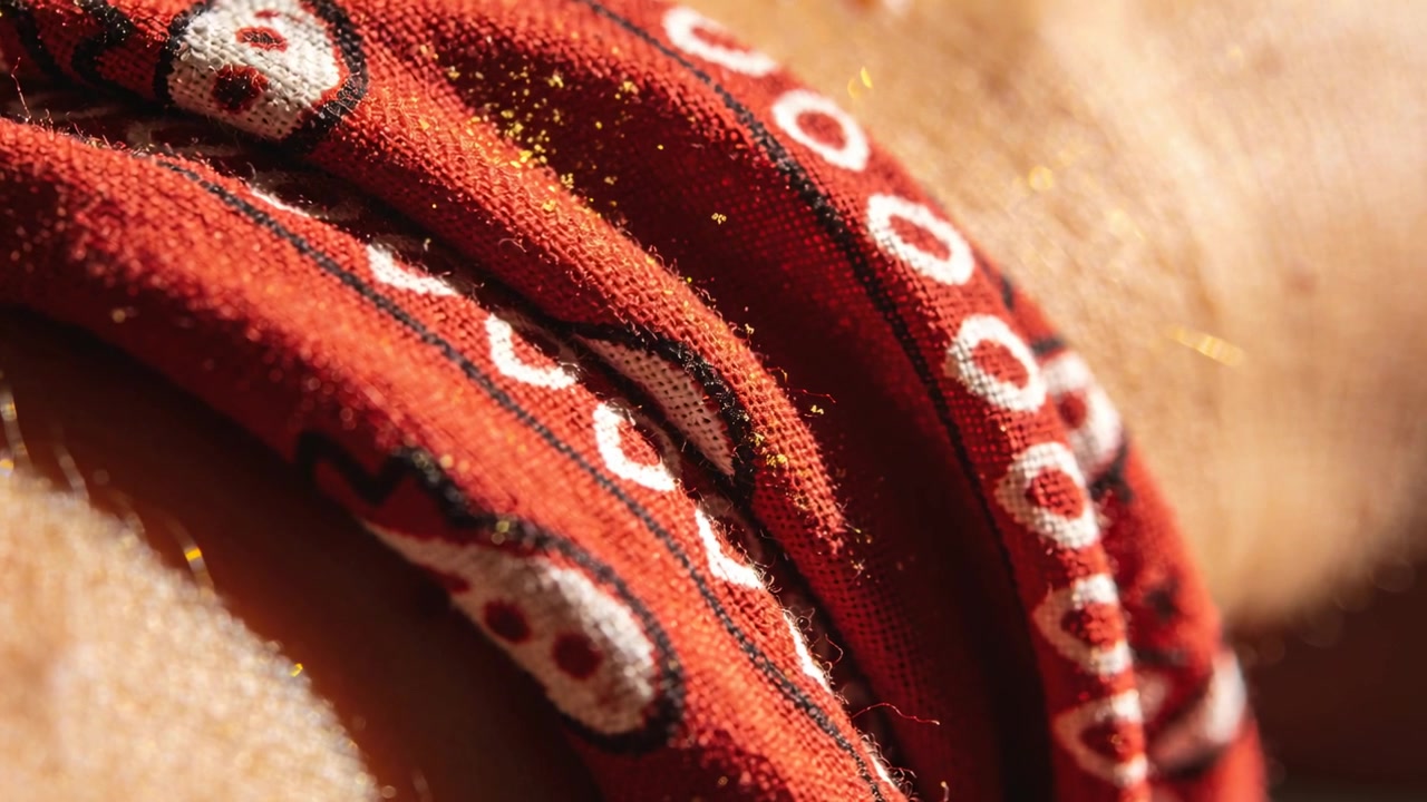 Una bandana rossa piegata si sposta premendo contro la pelle a casa, il respiro rivela pagliuzze d'oro.