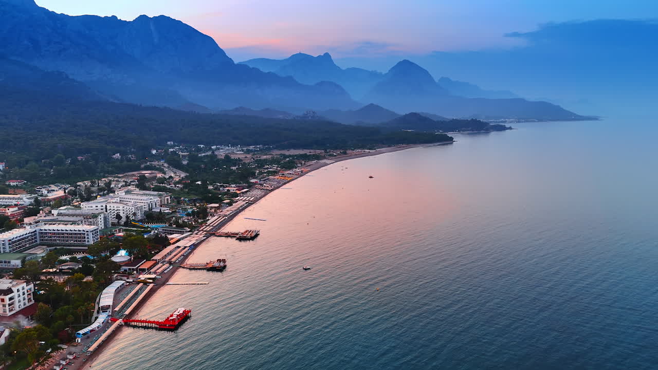 Coastal view at dusk over a serene bay. Dusk settles over a calm bay, revealing mountains, a coastline, and peaceful waters reflecting the soft colors