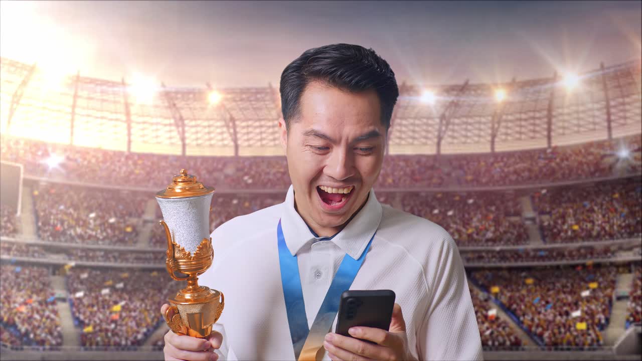 금메달과 트로피를 들고 스마트폰을 보고 스타디움에서 와우라고 말하는 아시아 남자의 클로즈업