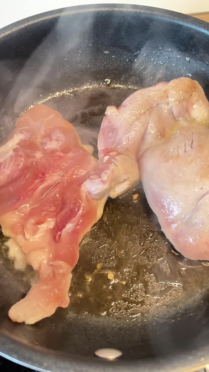 Due pezzi di pollo stanno cuocendo in una padella. La padella è nera e il pollo è rosa